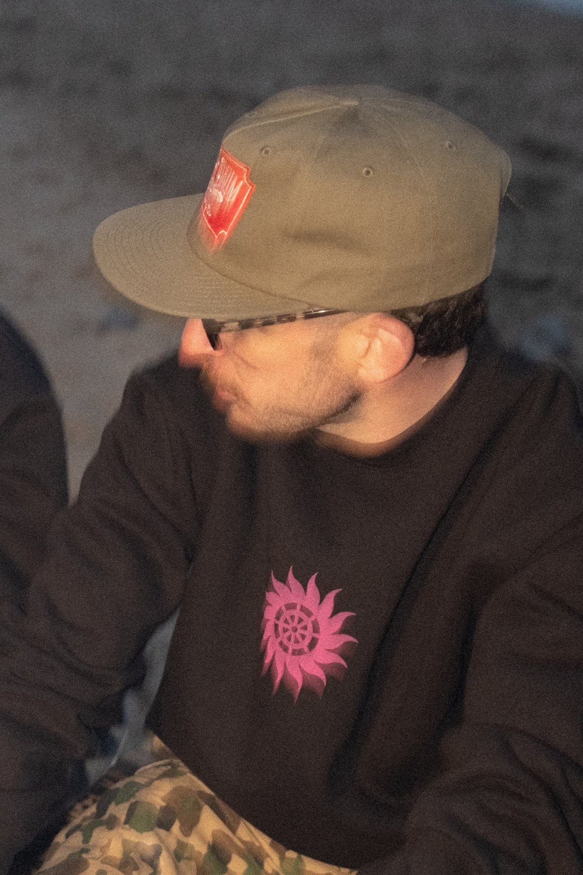 Side view of the army green Vintage Tiger 5 panel cap and red tiger patch, worn with a black Neon Sun Wheel sweatshirt