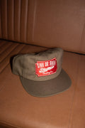 Vintage Tiger 5 panel cap in army green cotton canvas with red embroidered Sink Or Swim tiger patch, on a tan leather seat