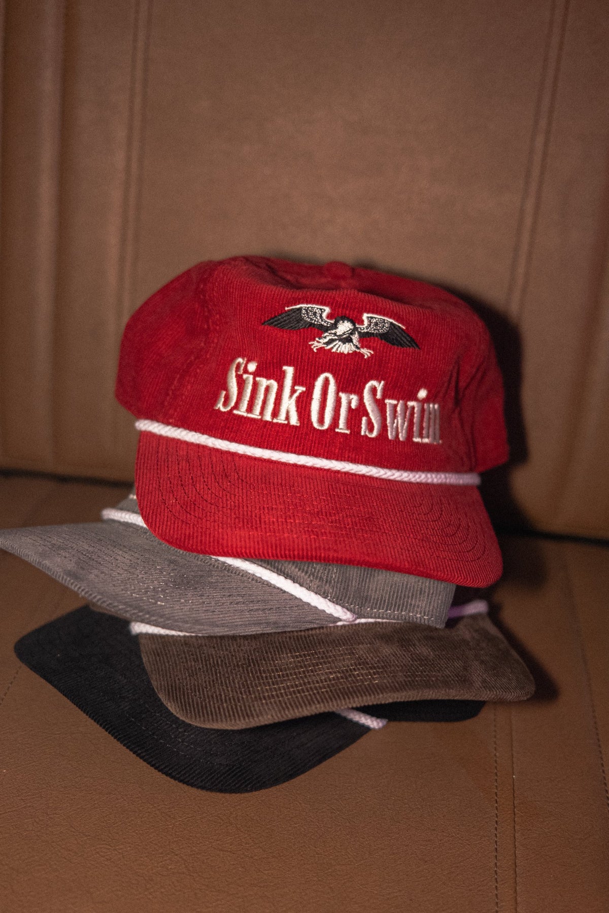 Vintage Eagle corduroy rope caps stacked in red, grey, brown and black, each with cream Sink Or Swim eagle embroidery
